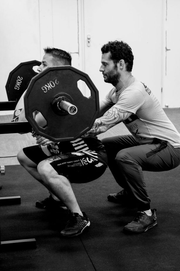 Personal Training Deventer - Tobias begeleid iemand met gewicht heffen in zijn gym.